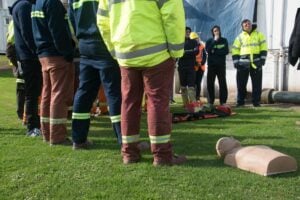 Construction workers in hi-vis gear attending an outdoor first aid and CPR training session with a manikin on the ground