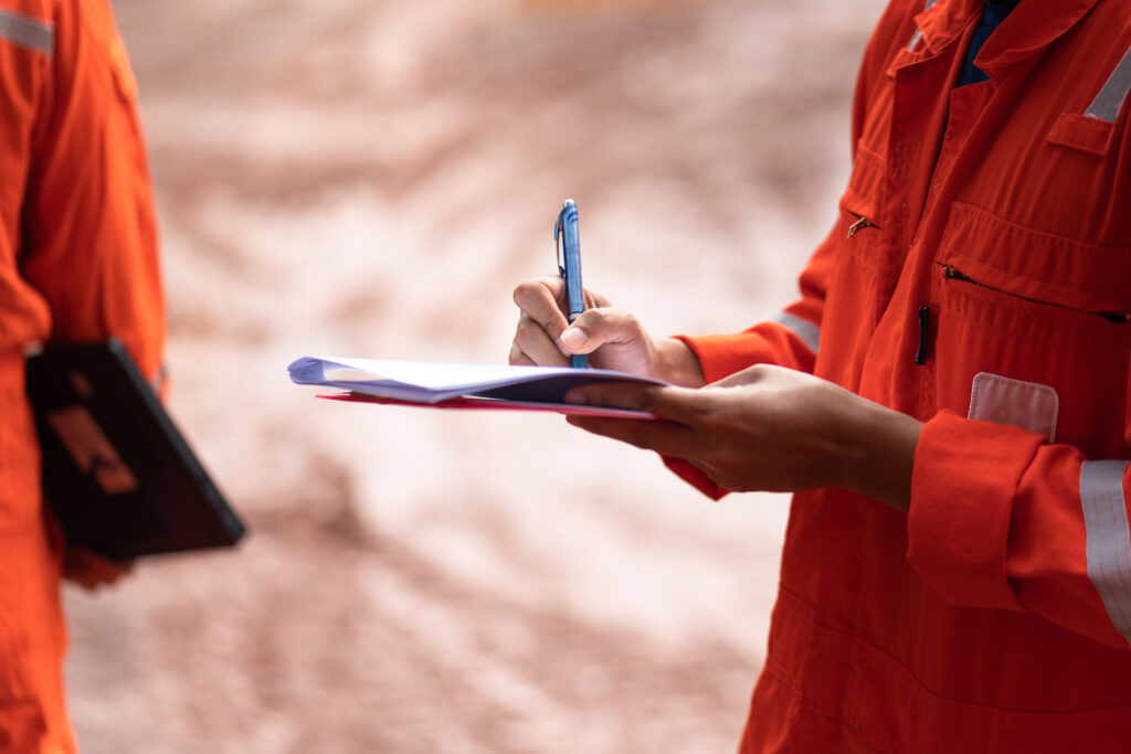 Action of safety officer is writing and check on checklist document during safety audit and inspection at drilling site operation. Industrial expertise occupation photo.