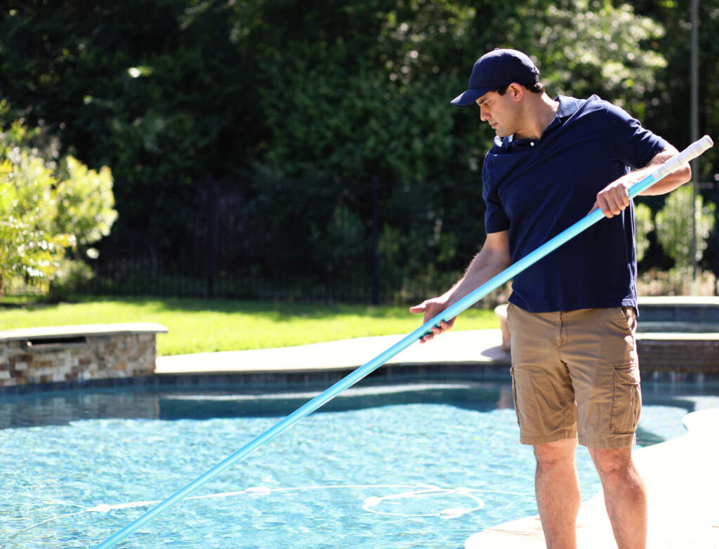 Pool technician cleaning outdoor swimming pool with vacuum pole